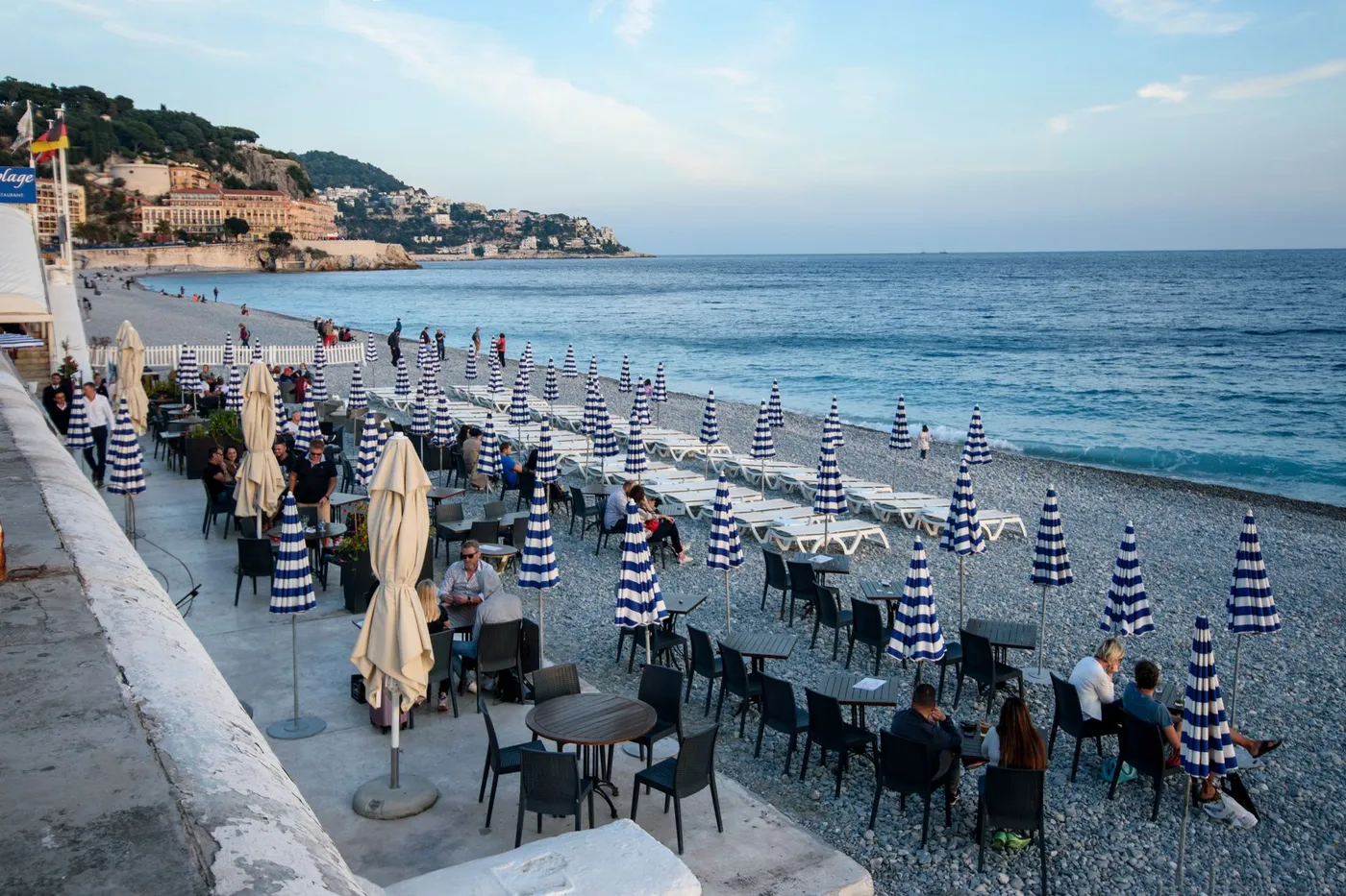 People enjoy a beachside cafe on the French Riviera with striped umbrellas and sea view.