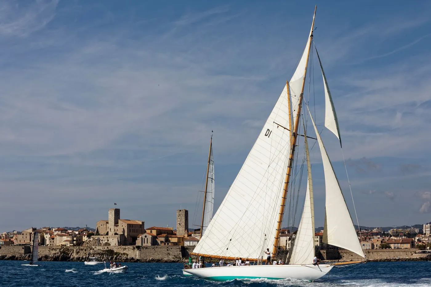 Sailboat gracefully gliding by the shores of Antibes, with a picturesque old town in the background.